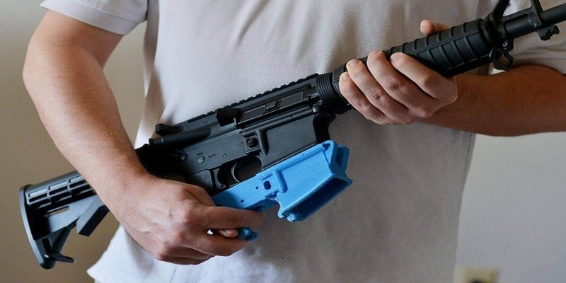 An AR15 rifle with a bright blue 3D printed "lower" reciever.